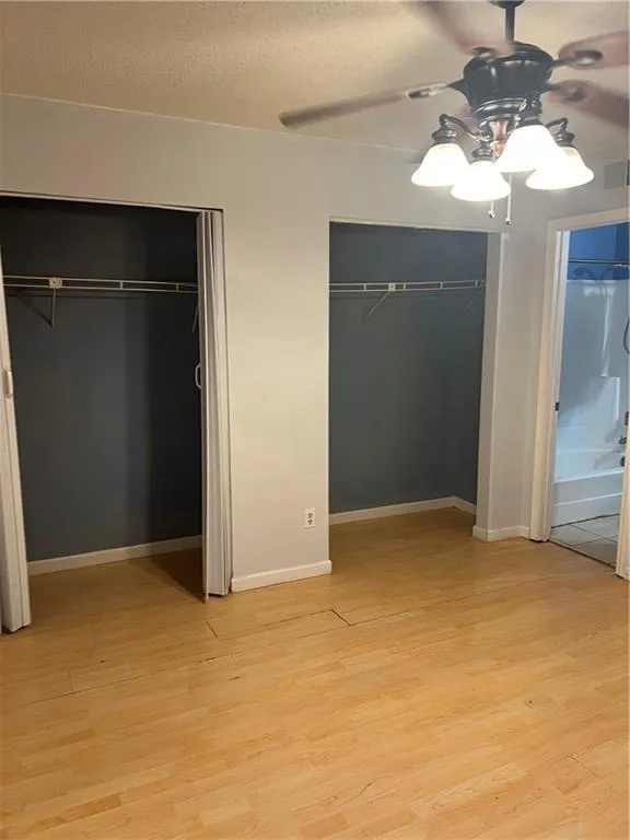 Unfurnished bedroom featuring multiple closets, light hardwood / wood-style floors, and ceiling fan