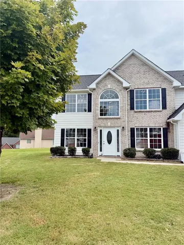 Two-story residence featuring a brick facade with shuttered windows, a white oval-lite entry door, and a prominent arched window on the second level
