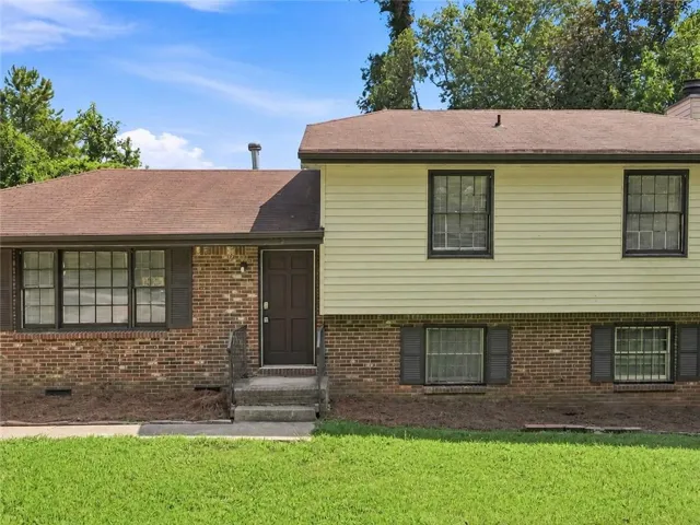 Brick and siding exterior featuring a multi-level design, brown asphalt shingle roof, dark entry door, and multiple windows with dark shutters