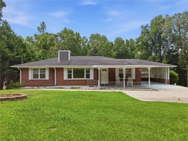 Brick ranch-style residence featuring a covered front porch with white railing, a two-car carport, and a dark shingle roof