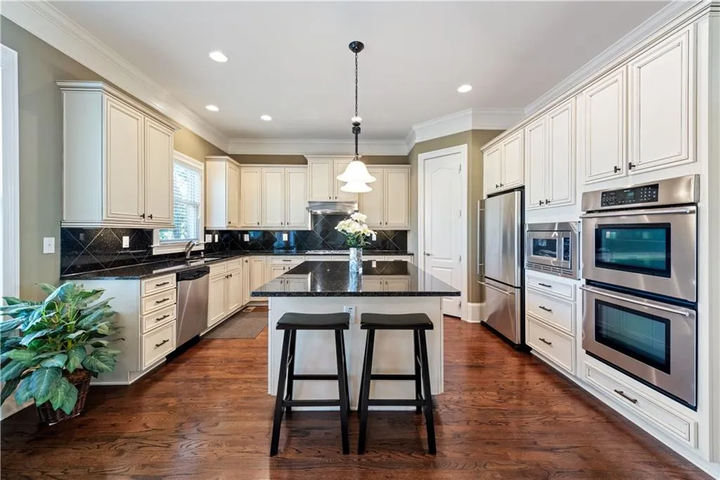 Kitchen featuring under cabinet range hood, a kitchen island, a sink, appliances with stainless steel finishes, and dark wood finished floors