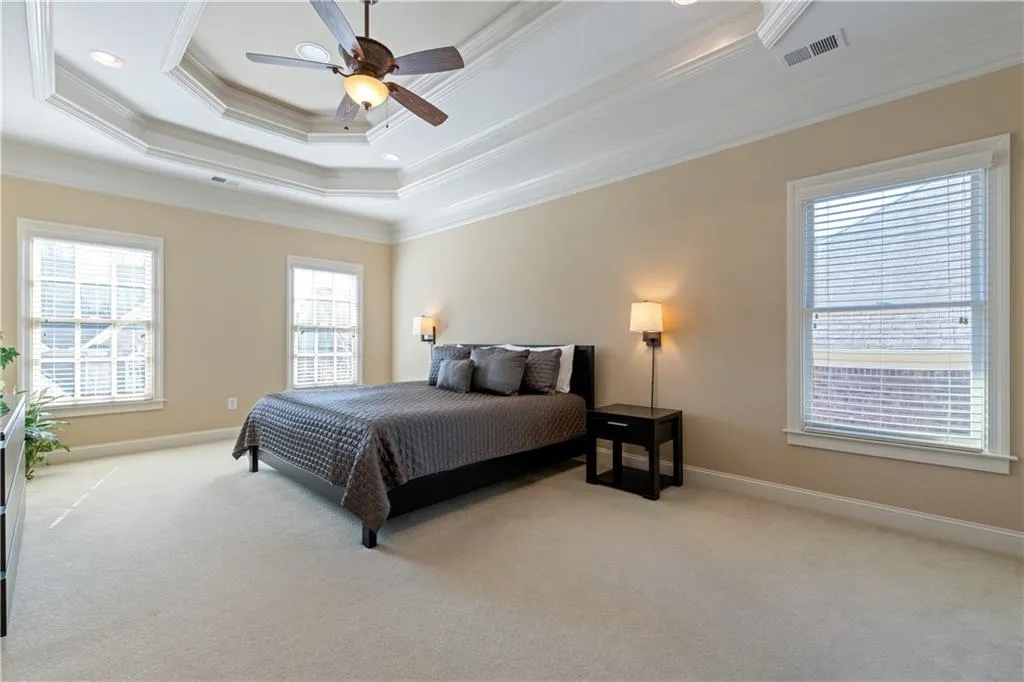 Bedroom featuring carpet floors, visible vents, baseboards, ornamental molding, and a tray ceiling