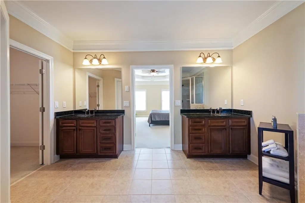 Ensuite bathroom featuring crown molding, two vanities, a sink, and tile patterned floors
