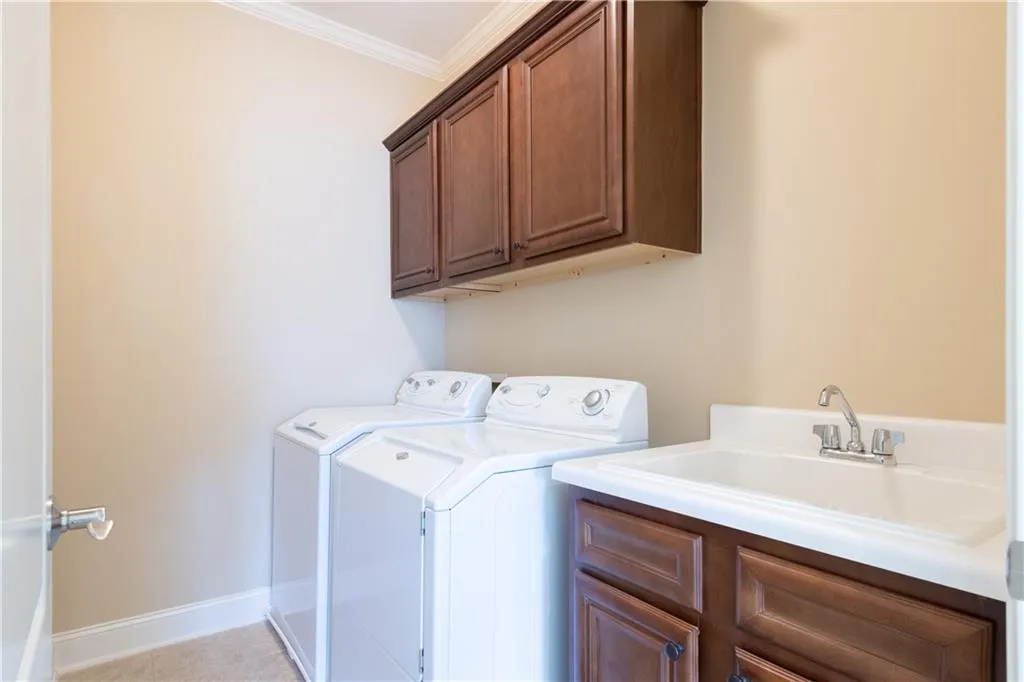 Laundry area featuring cabinet space, baseboards, washing machine and clothes dryer, crown molding, and a sink