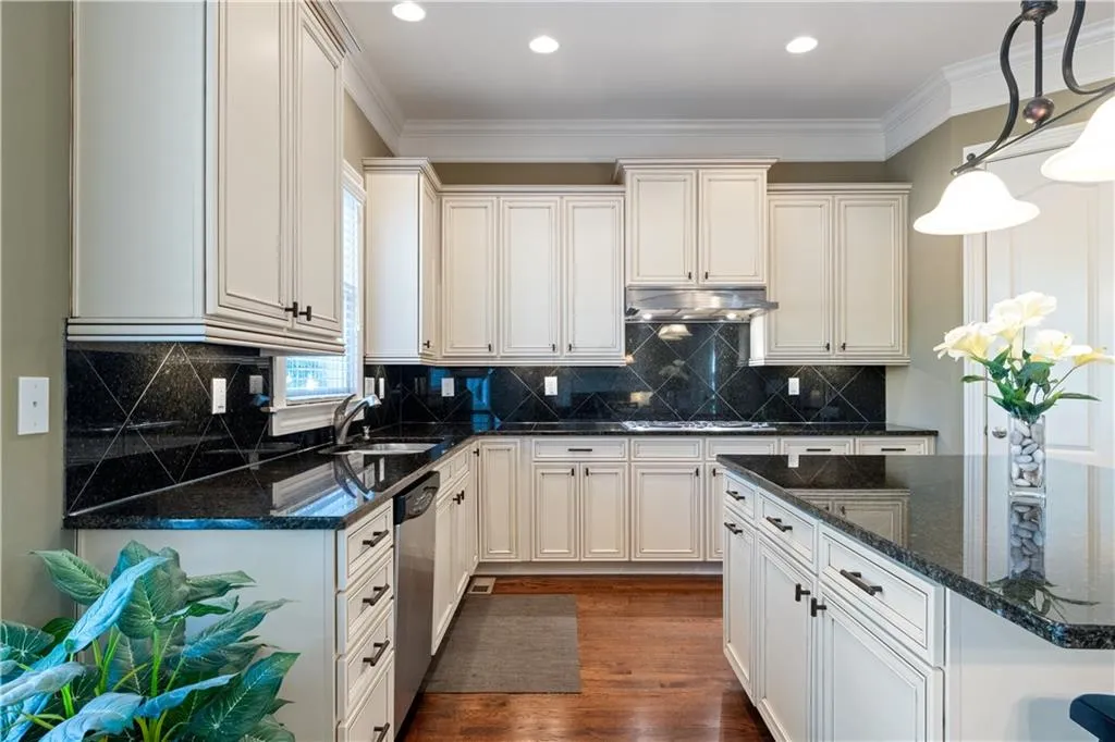 Kitchen featuring dark wood finished floors, crown molding, appliances with stainless steel finishes, a sink, and under cabinet range hood