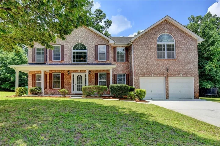 Brick facade residence featuring a two-story design with a front porch, a two-car garage, and an arched window