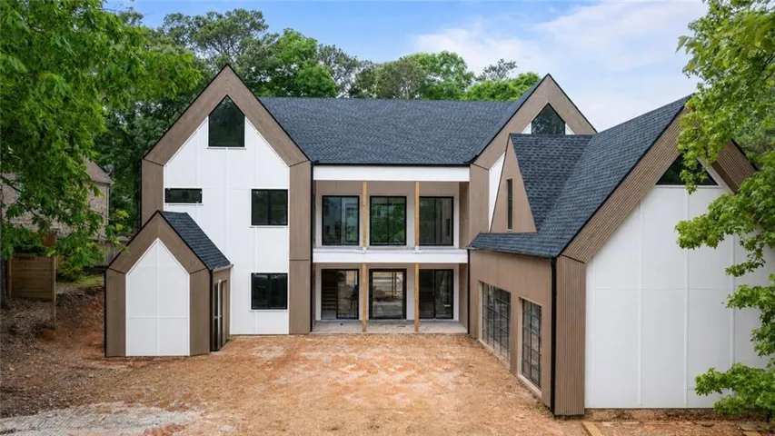 Contemporary architecture featuring a multi-gabled roofline, dark shingle roofing, contrasting white and brown panel siding, multiple black-framed windows, and a two-story covered balcony