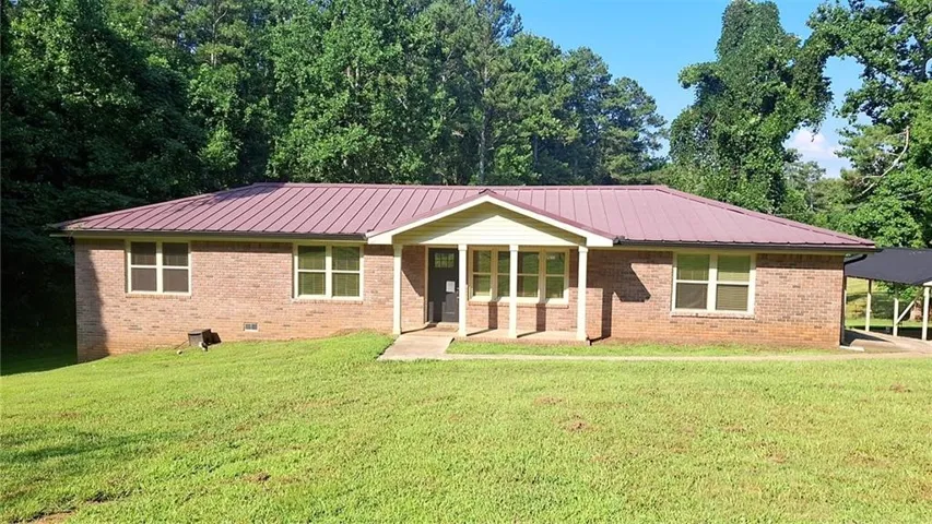 Brick ranch-style residence featuring a prominent metal roof, a covered entry porch, and an attached carport