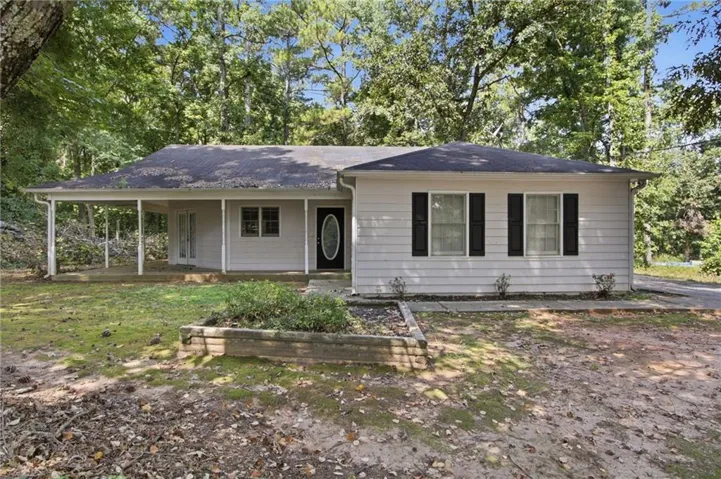 Ranch-style exterior with light-colored siding, black shutters, covered front porch, oval-paneled entry door, and a raised garden bed