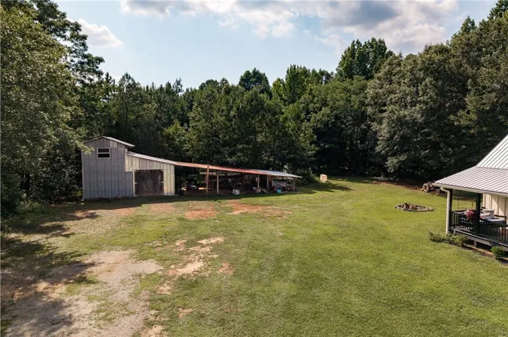 Expansive green lawn with a large barn featuring metal siding and an attached open-air lean-to structure
