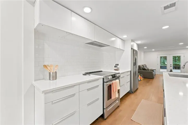 Modern kitchen featuring white flat-panel cabinetry, white quartz countertops, subway tile backsplash, and stainless steel appliances