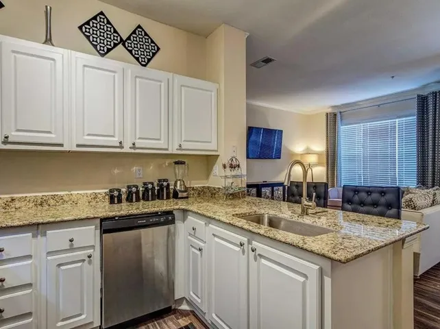 Kitchen with light stone counters, white cabinetry, dishwasher, a peninsula, and ornamental molding