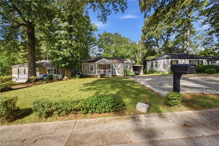 Manicured lawn with mature trees and a paved driveway leading to a carport