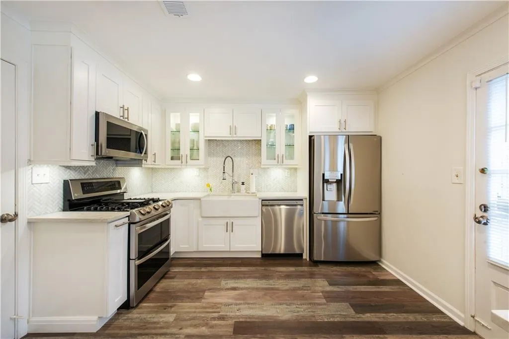 Kitchen with appliances with stainless steel finishes, dark wood-style floors, glass insert cabinets, light countertops, and white cabinetry