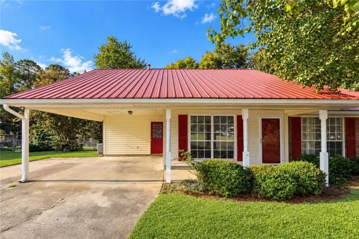 Red metal roof, covered carport, yellow siding, white porch columns, and red shutters