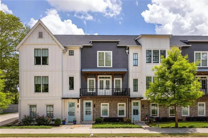 Contemporary townhome exterior featuring mixed material siding, dark-frame windows, light blue entry doors, and a second-story balcony with wrought iron railing
