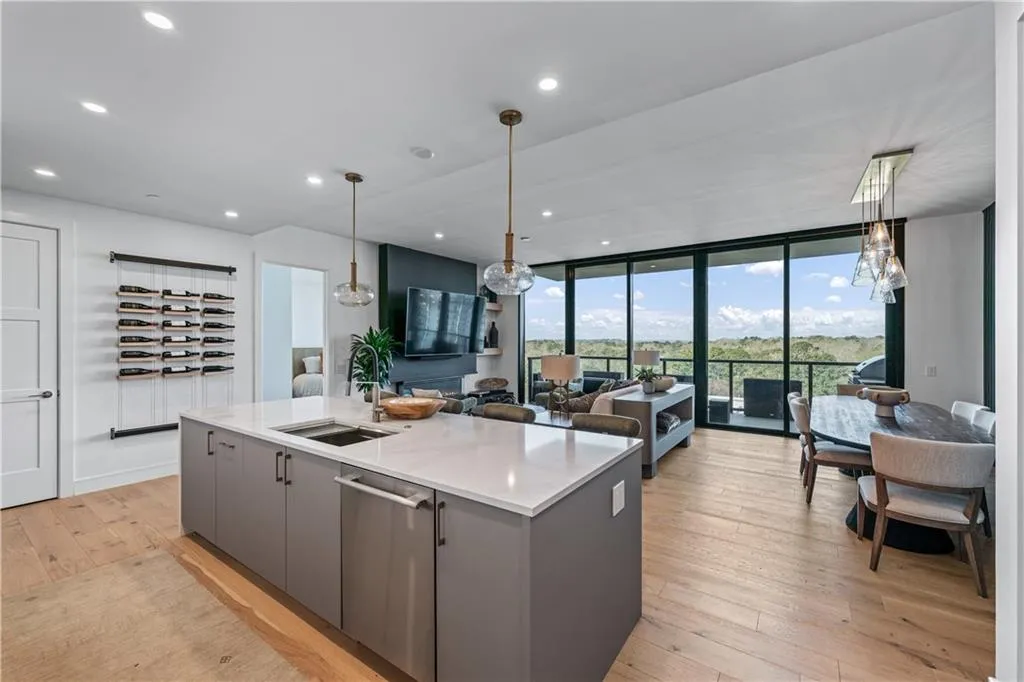 Kitchen with gray cabinetry, a center island with sink, stainless steel dishwasher, light wood-style floors, and open floor plan