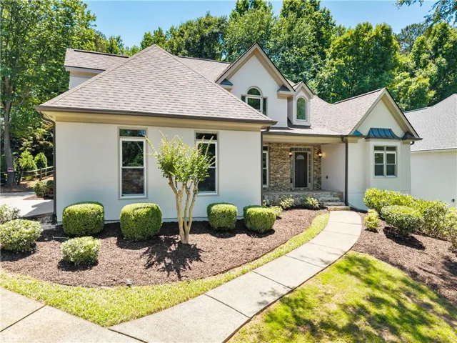 Stucco and stone exterior featuring a covered entry, arched dormer windows, and a concrete walkway