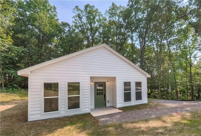 Single-story residence featuring white horizontal siding, a light green entry door, and a gravel driveway