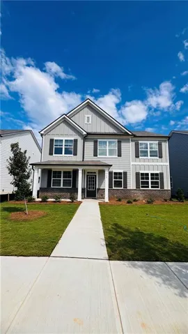 Two-story Colonial with gabled roofline and stone/composite exterior featuring multiple multi-pane windows, a covered front entry, and a concrete front walkway leading to an attached driveway
