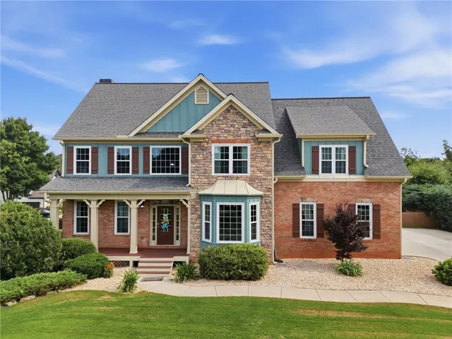 Brick and stone facade, architectural shingles, bay window, covered porch, and mature landscaping
