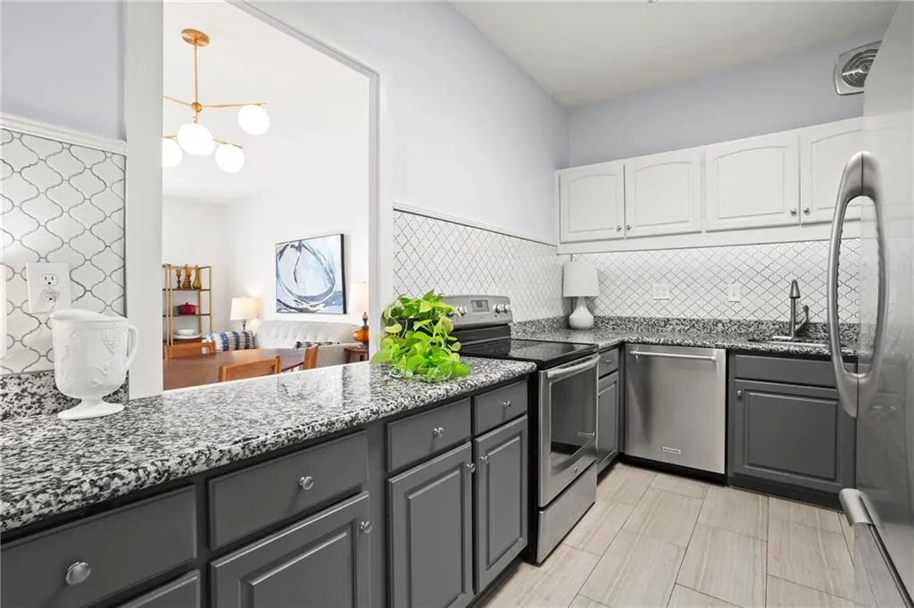 Kitchen with stainless steel appliances, gray cabinetry, white cabinets, dark stone counters, and a chandelier
