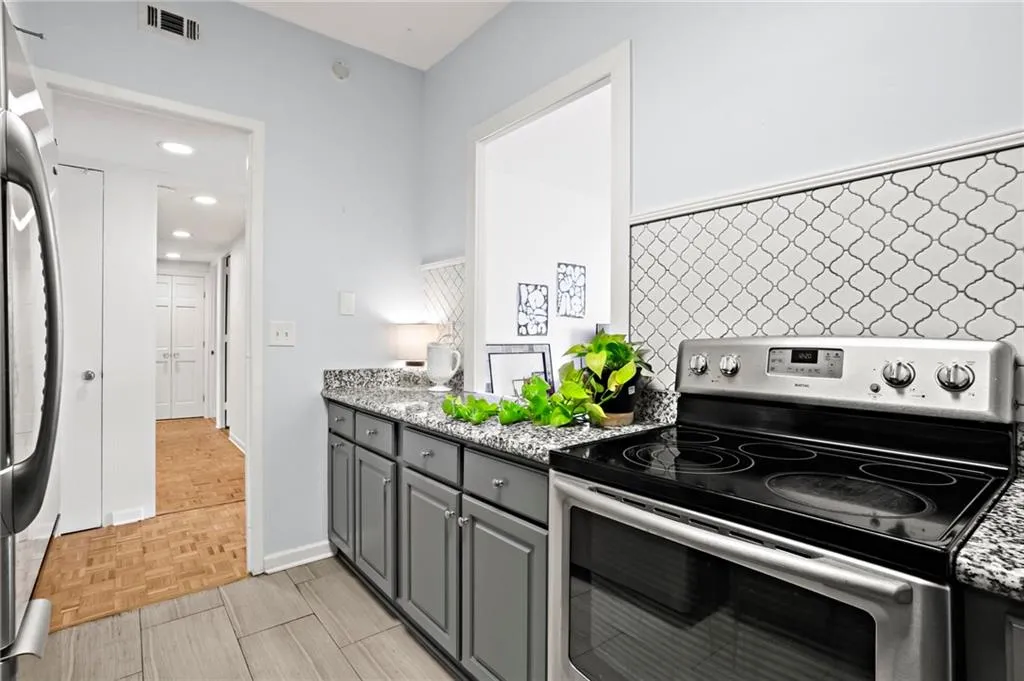 Kitchen with stainless steel electric range oven, gray cabinets, refrigerator, light stone counters, and recessed lighting
