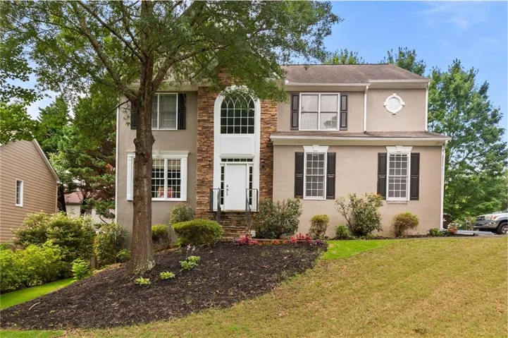 Two-story stucco and stone facade residence featuring an arched transom window above the entry, black louvered shutters, and a circular accent window