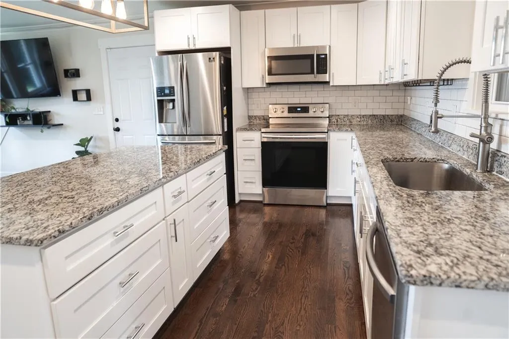 Kitchen with stainless steel appliances, tasteful backsplash, dark wood finished floors, white cabinets, and light stone counters