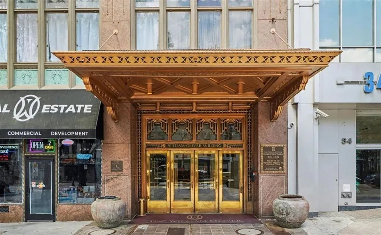 Ornate gold-finished entrance canopy with intricate detailing, featuring large brass-framed glass doors, a stone facade, and a decorative historic plaque