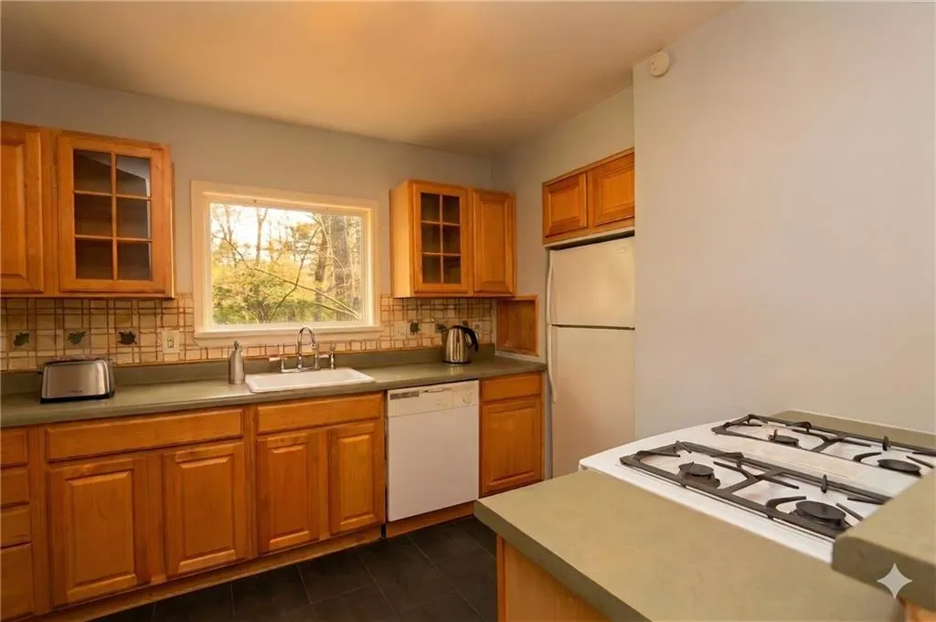 Kitchen with glass fronted cabinets, wood finish cabinets, white appliances, and dark tile patterned flooring