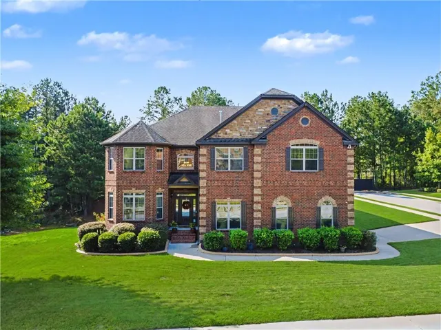Brick exterior with stone accents, mature landscaping, paved driveway, and multiple windows with shutters