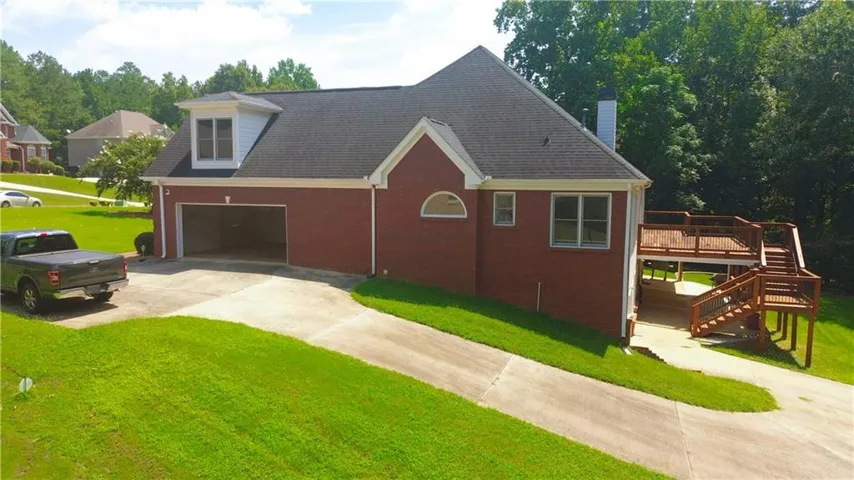 Two-car garage with concrete driveway, red brick exterior, dormer window, multi-level wood deck, and mature landscaping