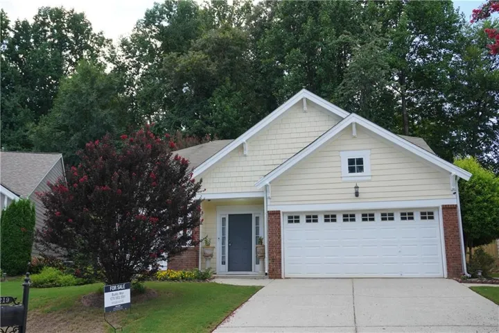 Light-toned horizontal siding with shake accents, brick detailing, and an attached garage with decorative windows
