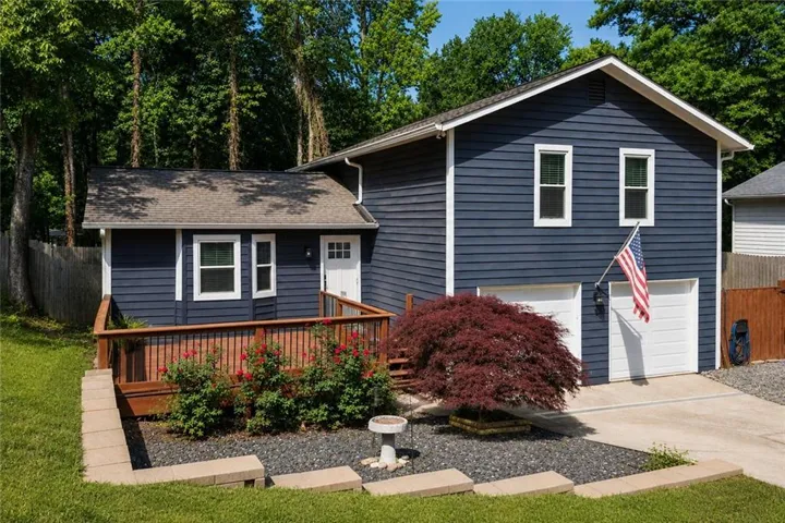 Exterior featuring blue siding, white trim, a wood deck, a two-car garage, and established landscaping
