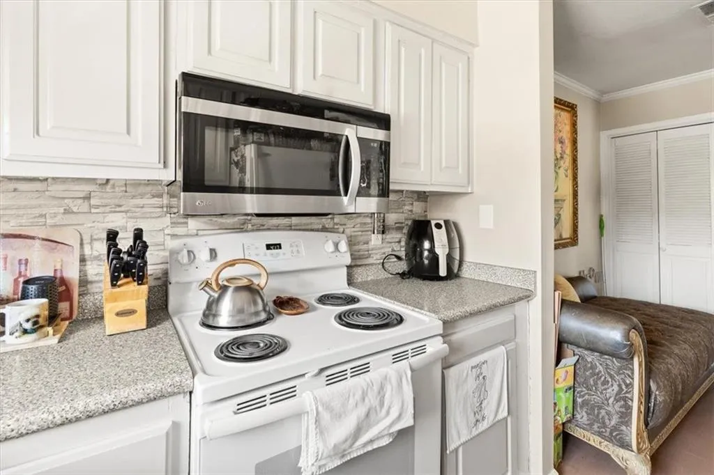 Kitchen featuring white range with electric stovetop, stainless steel microwave, ornamental molding, white cabinets, and decorative backsplash