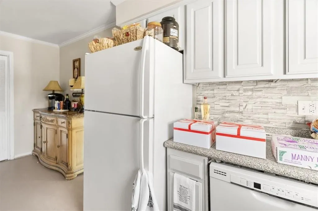 Kitchen featuring white appliances, crown molding, backsplash, and white cabinetry