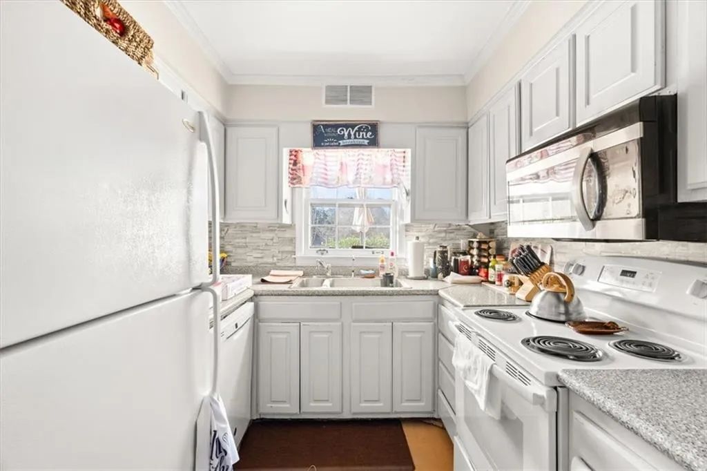 Kitchen with white appliances, light countertops, white cabinets, ornamental molding, and tasteful backsplash