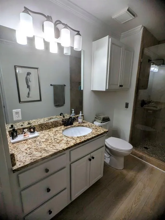 Bathroom with a shower with shower door, toilet, vanity, wood-type flooring, and ornamental molding