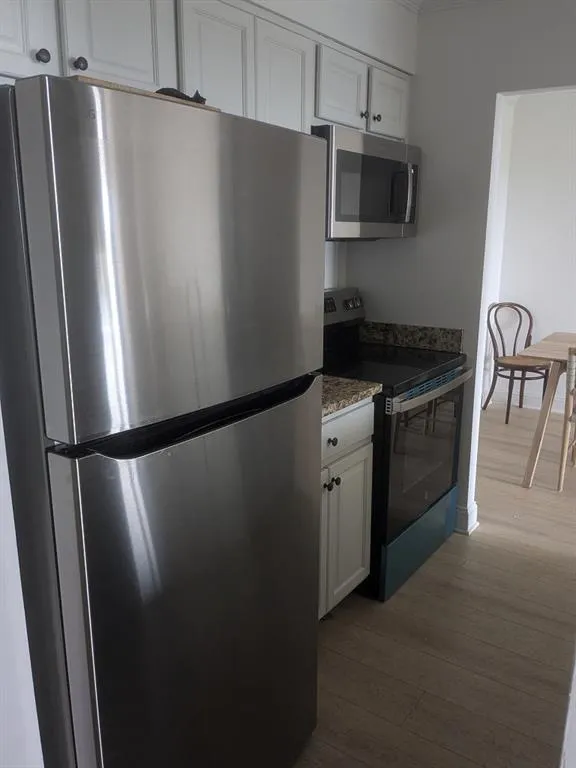 Kitchen with white cabinets, wood-type flooring, and appliances with stainless steel finishes