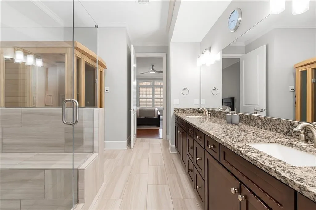 Bathroom featuring ensuite bath, double vanity, a shower stall, crown molding, and baseboards