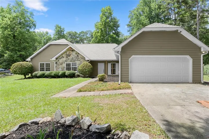 Exterior featuring a stone accent façade, horizontal siding, a two-car garage, front walk, and a landscaped yard