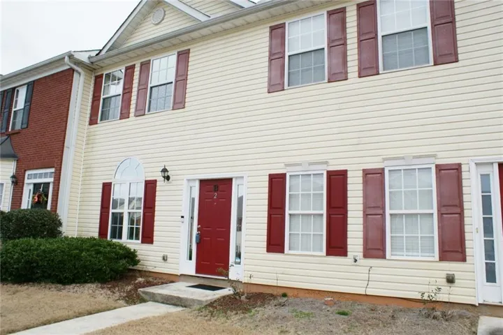 Cream-colored siding exterior with a red entry door, accented by red window shutters and white window frames