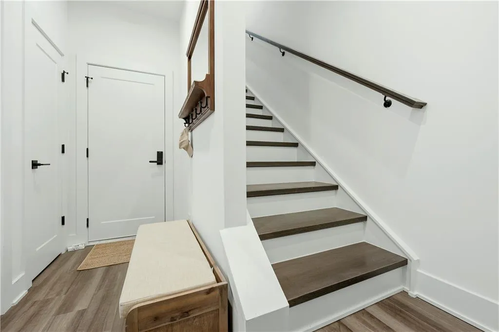 White interior doors with matte black hardware, wood-finish flooring, and a staircase featuring a dark wood handrail and matching treads