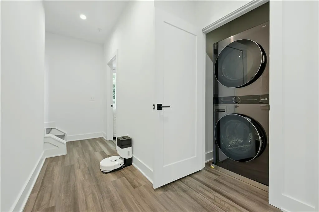 Integrated laundry center with stacked appliances, wood-finish flooring, white paneled doors, and recessed ceiling lighting