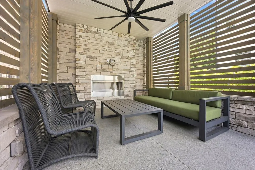 Covered patio featuring a stone-faced fireplace with a stainless steel insert, a ceiling-mounted fan, and slatted privacy screens