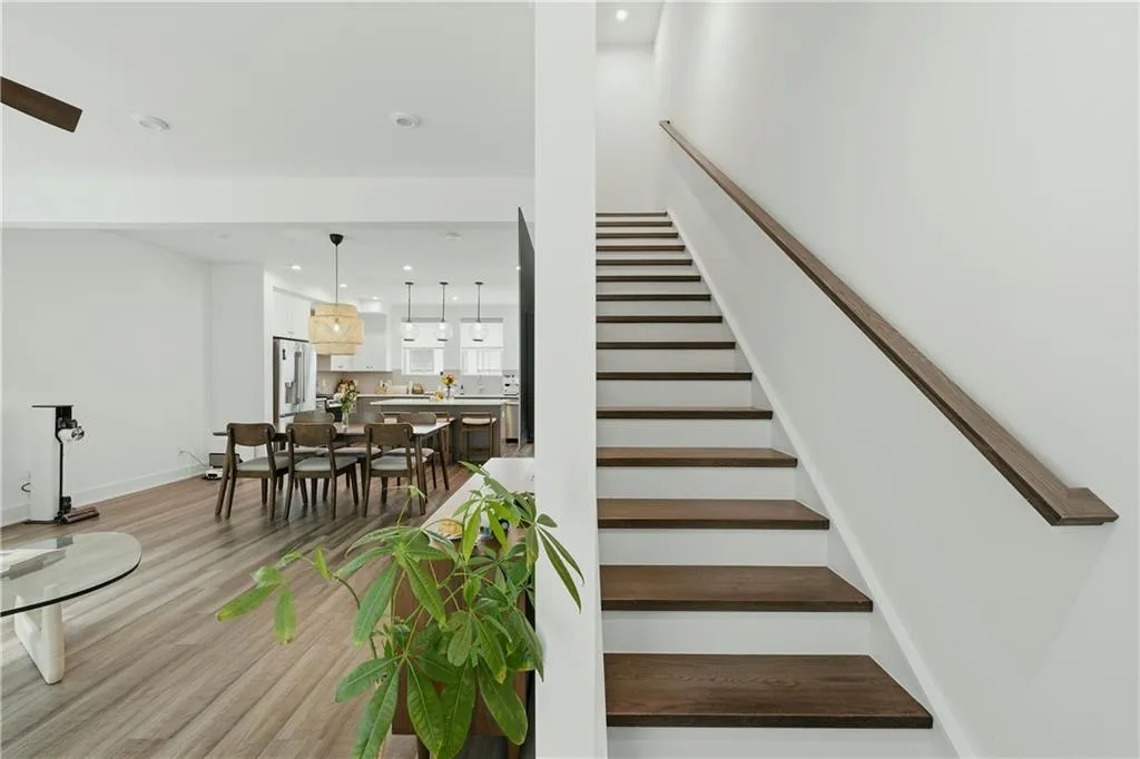 Open-concept living space with wood-finish flooring, recessed lighting, and a modern staircase featuring a wood handrail