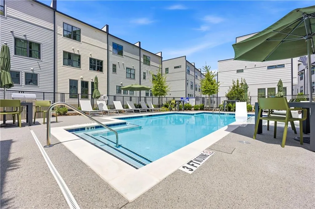 In-ground pool with integrated steps, surrounded by a textured concrete deck, and bordered by a metal fence