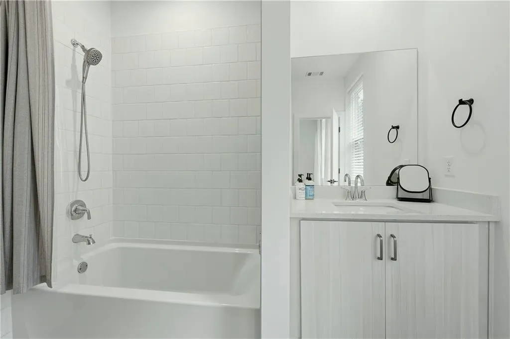 White subway tile shower surround, chrome shower fixtures, white bathtub, wood-finish vanity with double cabinet doors, and white countertop