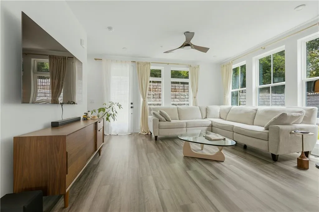 Spacious living area featuring wood-finish flooring, a contemporary ceiling fan, and multiple windows